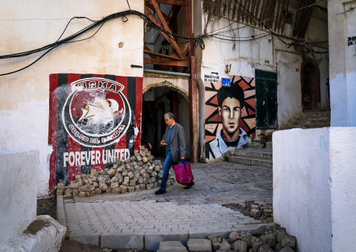 Man passing near murals of football and revolution in the casbash, North Africa, Algiers, Algeria