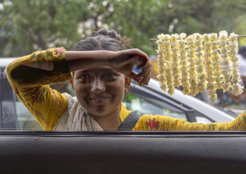 Bangladeshi girl looking thru car glass to sell jasmin garlands, Dhaka Division, Dhaka, Bangladesh