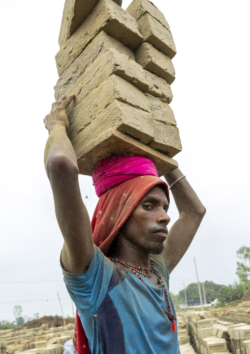 Hijra carrying bricks on his head at a brick factory, Sylhet Division, Bahubal, Bangladesh