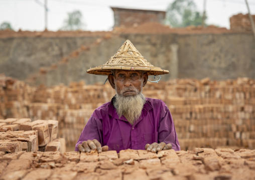 Portrait of a senior male worker with a bamboo hat in a brick factory, Sylhet Division, Bahubal, Bangladesh