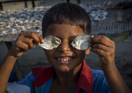 Bangladeshi boy putting dry fishes in front of his eyes to joke, Chittagong Division, Cox's Bazar Sadar, Bangladesh