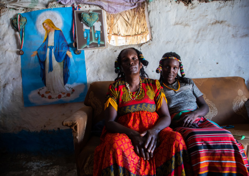 Portrait of Kunama tribe women with traditional hairstyles in front of a virgin mary poster, Gash-Barka, Barentu, Eritrea