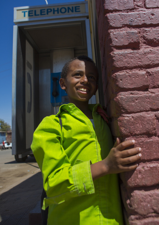 Eritrean boy with school uniform in front of a public phone, Central Region, Asmara, Eritrea