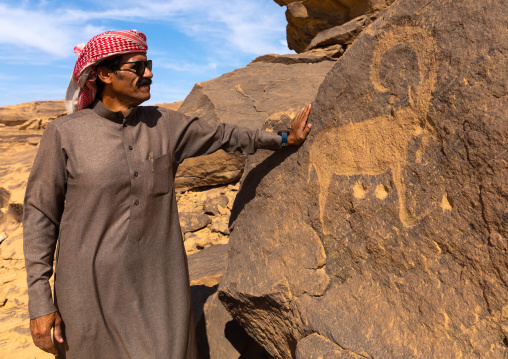 Saudi man in front off petroglyphs on a rock depicting ibex, Najran Province, Thar, Saudi Arabia