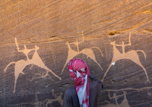 Saudi man in front of petroglyphs on a rock depicting hunters riding horses, Najran Province, Thar, Saudi Arabia