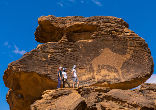 Tourists in front of Jabal Al-Mawaqi giant camel rock art, Najran Province, Thar, Saudi Arabia