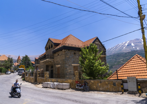 Man on a scooter passing in front of an old lebanese house, North Governorate, Bsharri, Lebanon