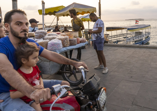 Man with his daughter riding his motorcycle along the sea, North Governorate, Tripoli, Lebanon