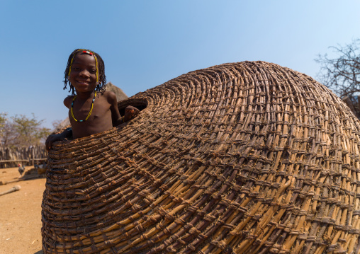 Muhacaona tribe girl inside a giant basket used to keep the corn, Cunene Province, Oncocua, Angola