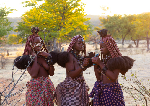 Himba tribe women looking at polaroids, Cunene Province, Oncocua, Angola