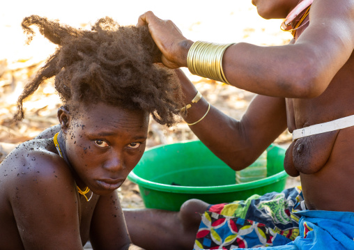 Nguendelengo tribe woman puting oil in her hair to make traditional buns, Namibe Province, Capangombe, Angola