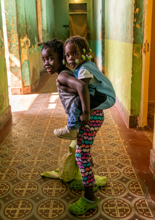 Angolan girl carrying her little sister on her back in their apartement, Namibe Province, Namibe, Angola