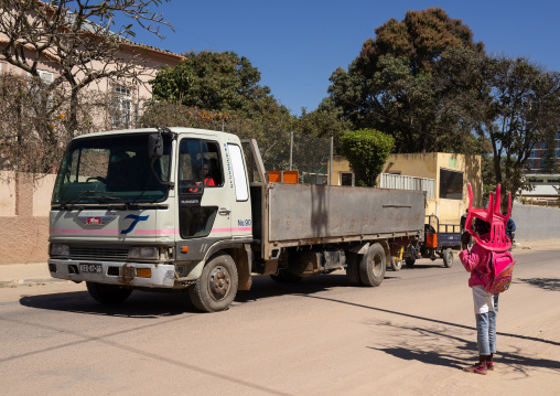 Angolan girl crossing a road while carrying her own chair to go to school, Huila Province, Lubango, Angola