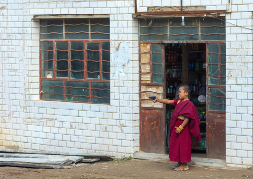 Tibetan child monk playing with a fake gun toy in Shachong monastery, Qinghai Province, Wayaotai, China