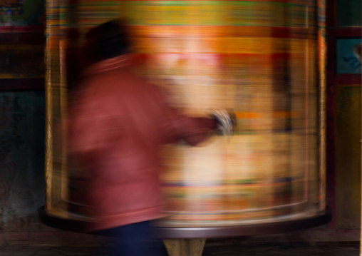 Tibetan pilgrim turning huge prayer wheel in Labrang monastery, Gansu province, Labrang, China