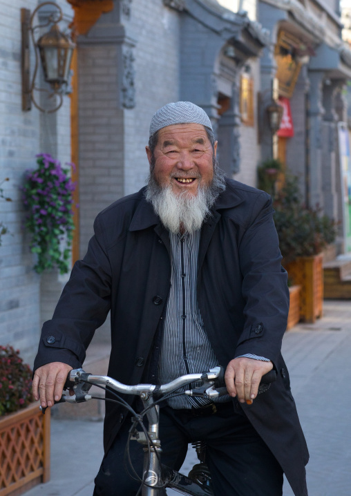 Smiling hui muslim man riding a bicycle in the street
, Gansu province, Linxia, China