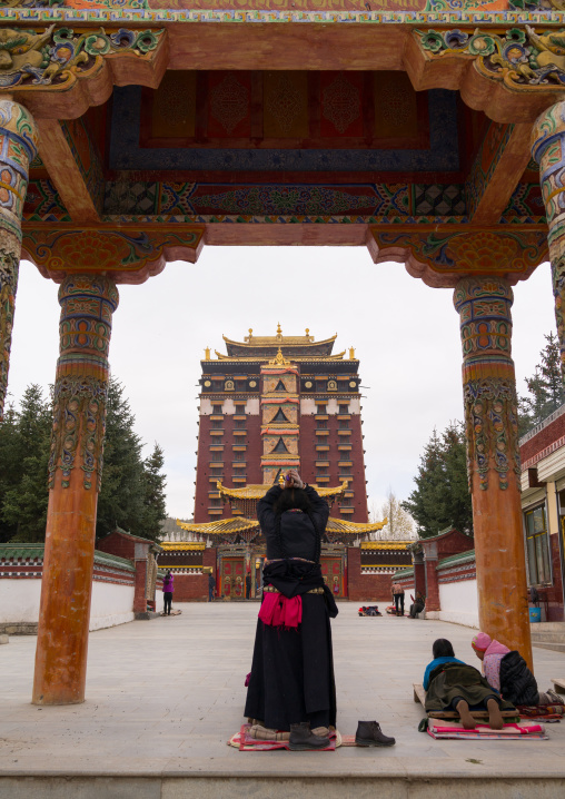 Tibetan pilgrims praying and prostrating in front of Hezuo monastery and its milarepa tower, Gansu province, Hezuo, China