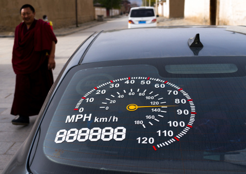 Monk passing in front of a car with a a speedometer on the windshield, Gansu province, Labrang, China