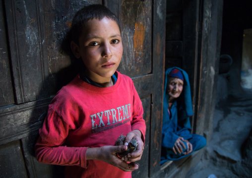 Afghan boy holding a bird in his hands and his grand mother in a pamiri house, Badakhshan province, Qazi deh, Afghanistan