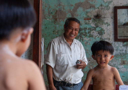 A boy having his hair cut by a man in a salon, Phnom Penh province, Phnom Penh, Cambodia