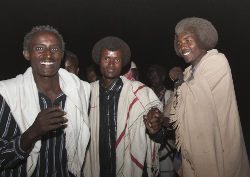 Night Shot Of Three Smiling Karrayyu Tribe Men In Traditional Clothes And Gunfura Hairstyle During Gadaaa Ceremony, Metahara, Ethiopia