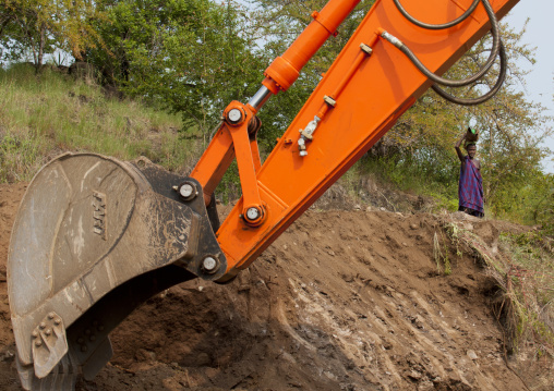 Indigenous Woman And Mechanical Digger Arm On Coated Road  Construction Work In Mago Park Omo Valley Ethiopia