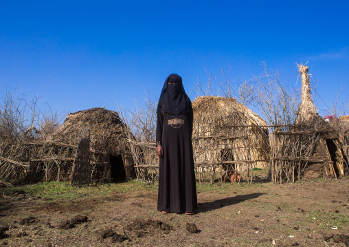 An ethiopian oromo woman dressed in black burqa stands in front of her hut, Amhara region, Artuma, Ethiopia