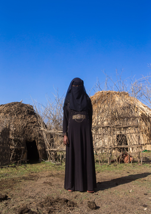 An ethiopian oromo woman dressed in black burqa stands in front of her hut, Amhara region, Artuma, Ethiopia