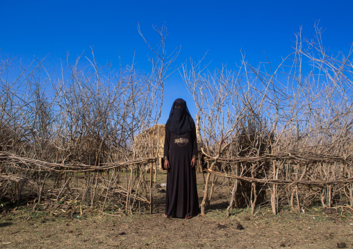 An ethiopian oromo woman dressed in black burqa stands in front of her hut, Amhara region, Artuma, Ethiopia