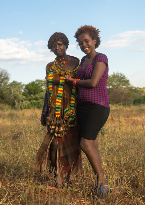 Hamer tribe woman with a hamer friend in western clothes attending a bull jumping ceremony, Omo valley, Turmi, Ethiopia