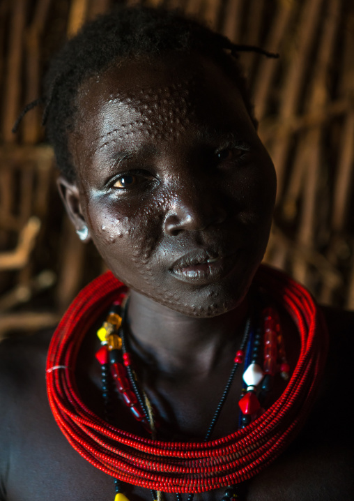 Toposa tribe woman with scarified face and red necklaces, Omo valley, Kangate, Ethiopia