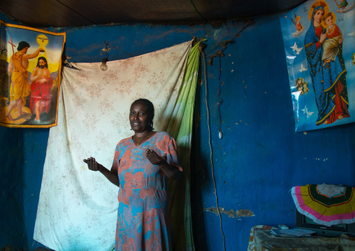 Woman inside her house decorated with religious posters, Omo valley, Jinka, Ethiopia