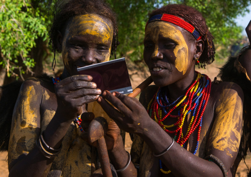 Dassanech tribe women looking polaroid pictures of themselves, Omo valley, Omorate, Ethiopia