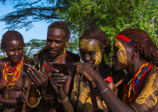 Dassanech tribe women looking polaroid pictures of themselves, Omo valley, Omorate, Ethiopia