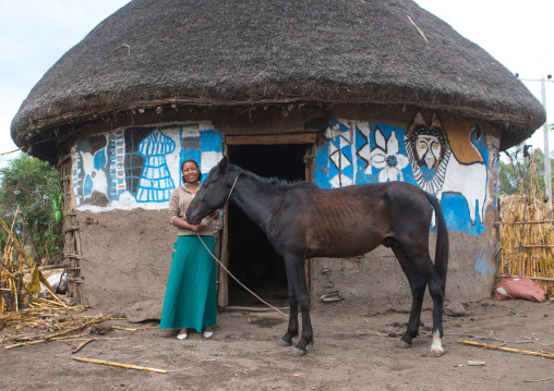 Ethiopia, Kembata, Alaba Kuito, ethiopian woman standing in front of her traditional painted house with a horse