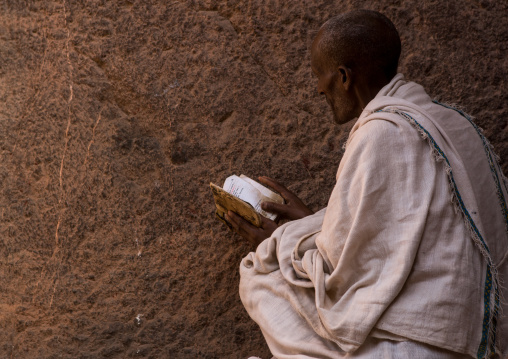 Lonely ethiopian orthodox man praying with a bible, Amhara region, Lalibela, Ethiopia