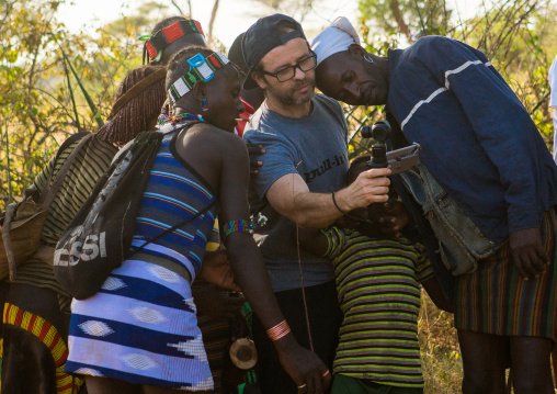 European tourist showing the screen of his camera to hamer tribe people, Omo valley, Turmi, Ethiopia