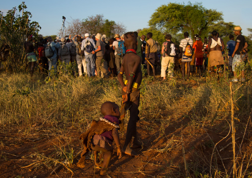 Hamer tribe children looking a group of tourists taking pictures of a bull jumping, Omo valley, Turmi, Ethiopia