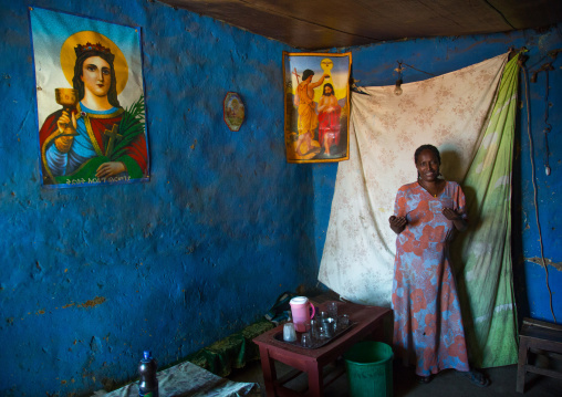 Woman inside her house decorated with religious posters, Omo valley, Jinka, Ethiopia