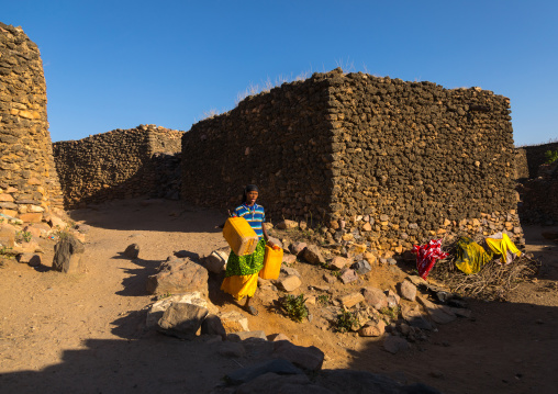 Argoba woman carrying water in jericans in a traditional stone houses cliff-top village, Harari Region, Koremi, Ethiopia