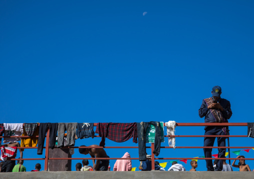 Ethiopian policeman looking at his mobile phone while people dry their clothes after the holy bath during Timkat festival, Amhara region, Lalibela, Ethiopia