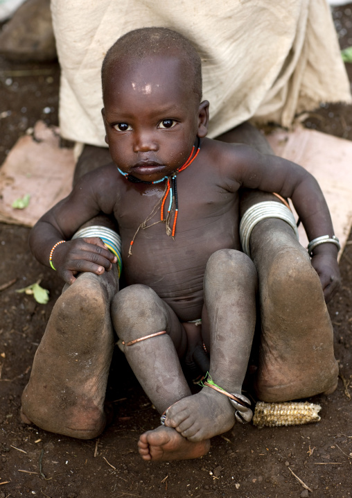 Young Suri Boy Sitting Between His Mother S Feet, Turgit Village, Omo Valley, Ethiopia