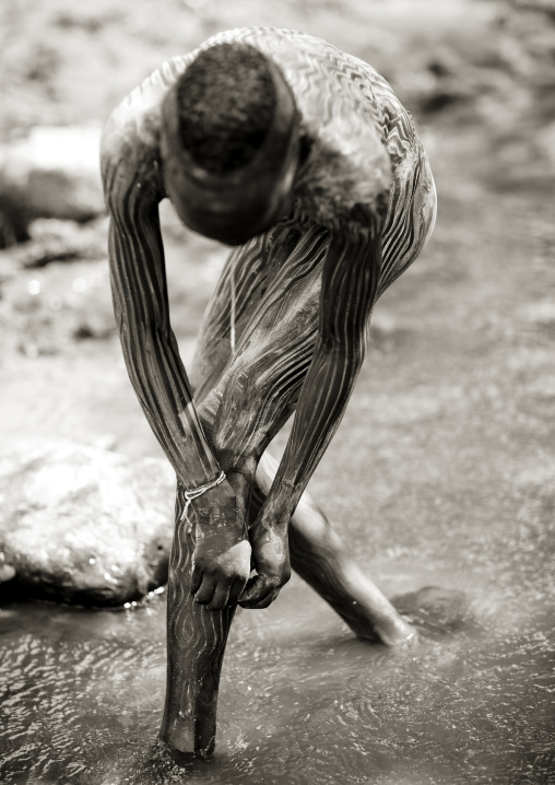 Suri man painting his body with clay in a river, Turgit village, Omo valley, Ethiopia