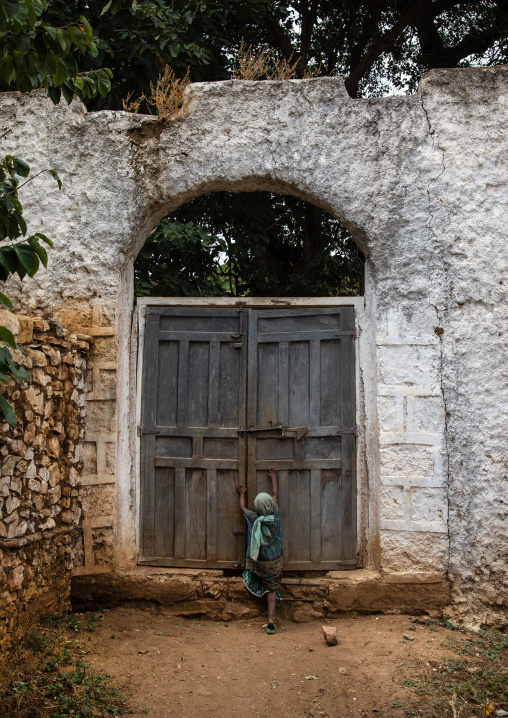 Girl trying to open the huge door of a muslim holy site, Harari Region, Harar, Ethiopia