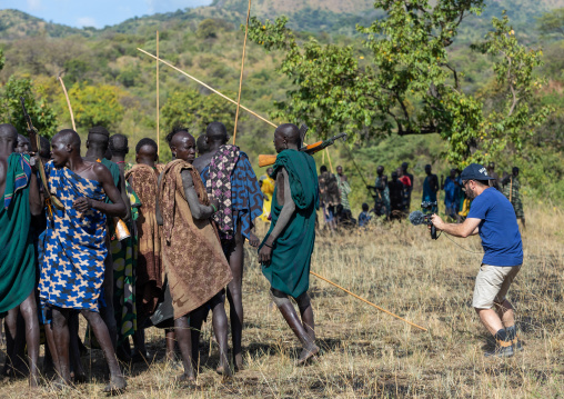 Western tourist filming suri tribe warriors during a donga stick fighting ritual, Omo valley, Kibish, Ethiopia