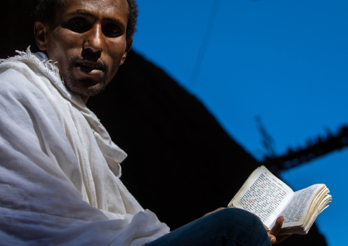 Orthodox man praying with a bible, Amhara Region, Lalibela, Ethiopia