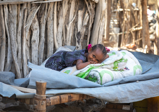 Ethiopian girl resting on a bed in front of her house, Afar Region, Assayta, Ethiopia