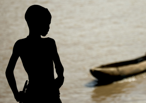 Silhouette Of A Kid Looking At Trunk Boat Used To Cross The Omo River, Omorate, Omo Valley, Ethiopia