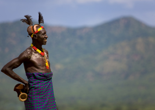 Portrait Of A Smiling Karo Tribe Man With Mud Bun And Headrest With Mountains In The Backgroung, Korcho Village, Omo Valley, Ethiopia