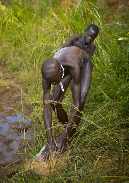 Man from Suri tribe receiving help to decorate his body with paintings, Tulgit, Omo valley, Ethiopia